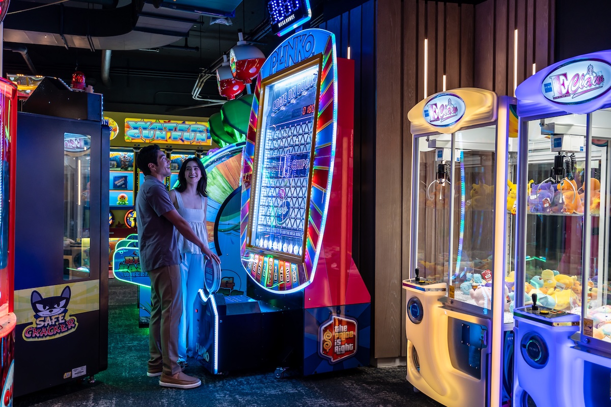 A man and a woman play at an arcade machine in an arcade.