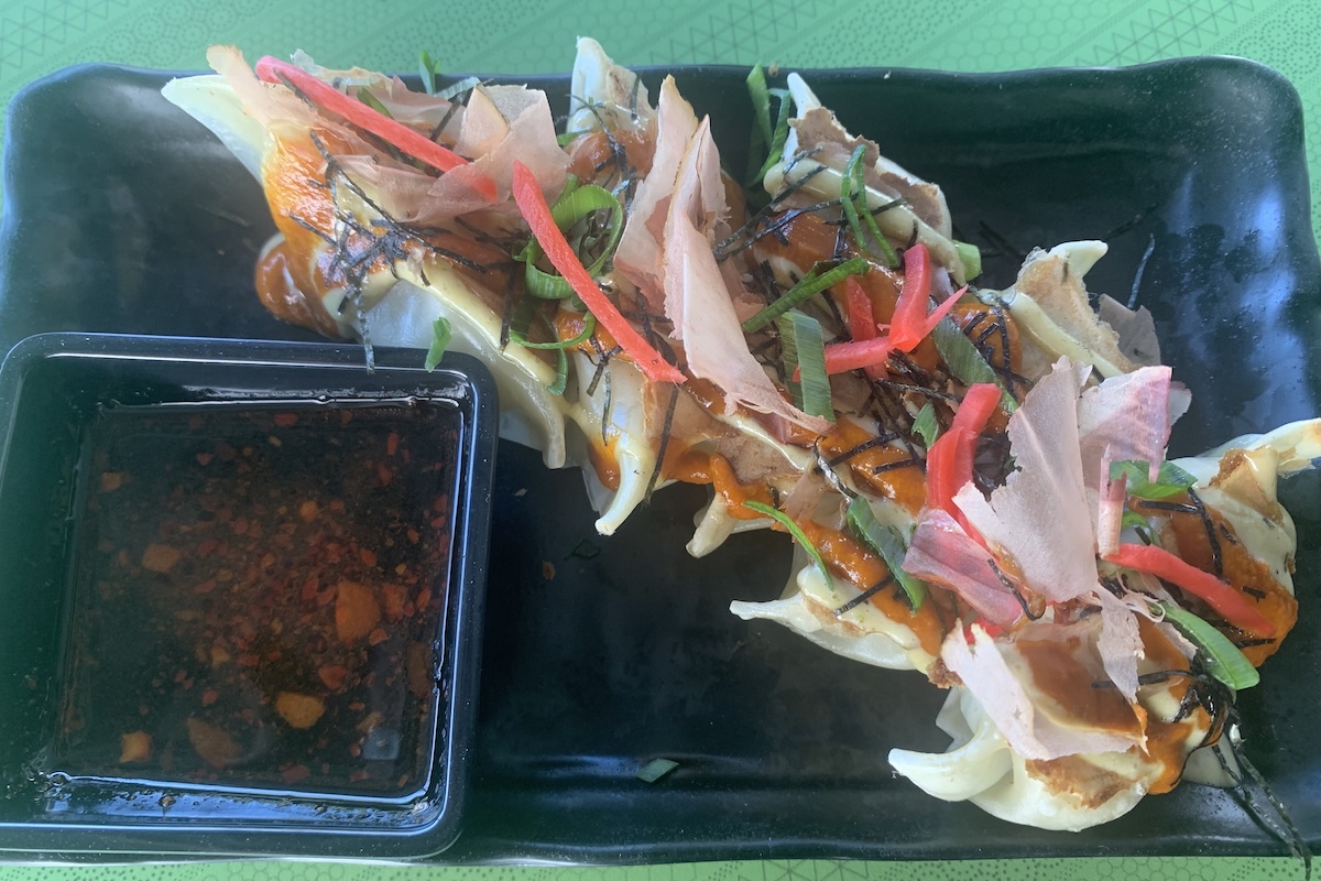 A plate of dumplings topped with carrots, green onions, sauce and thin slices of something pink.
