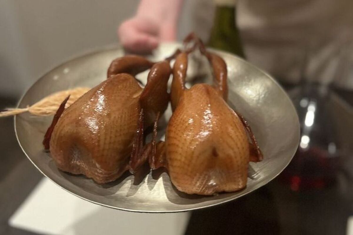 A man holds a silver plate with two roasted poultries.