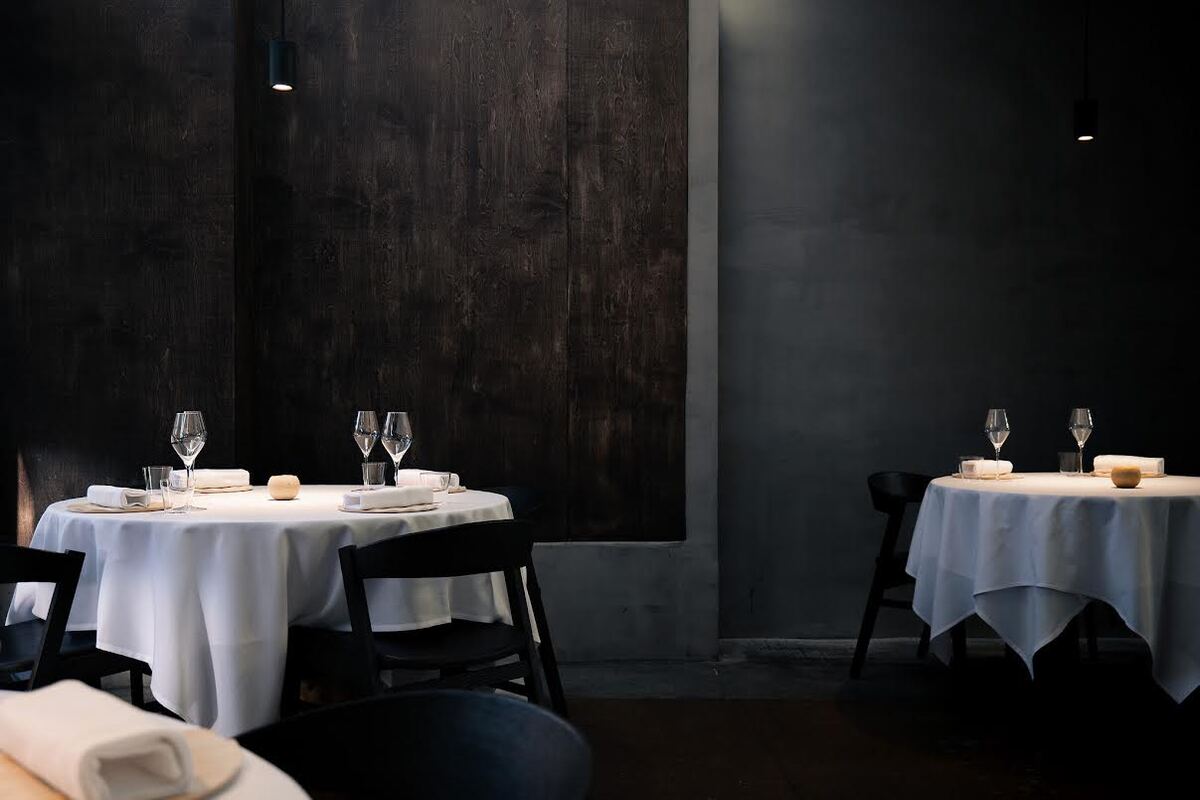 Dark wooden dark with round tables that have white table clothes and are set for guests.