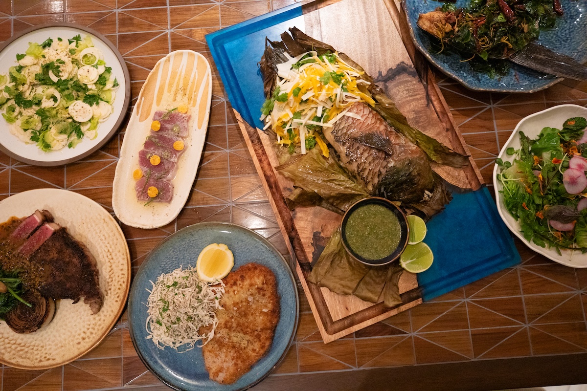 An overhead shot of plates with various dishes including salads, meat and other sides.