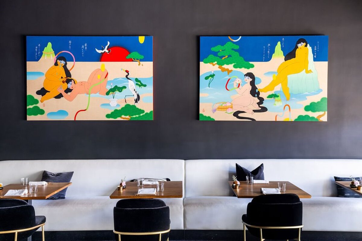 White fabric booth with small tables, black chairs and colorful art hanging on the wall behind.