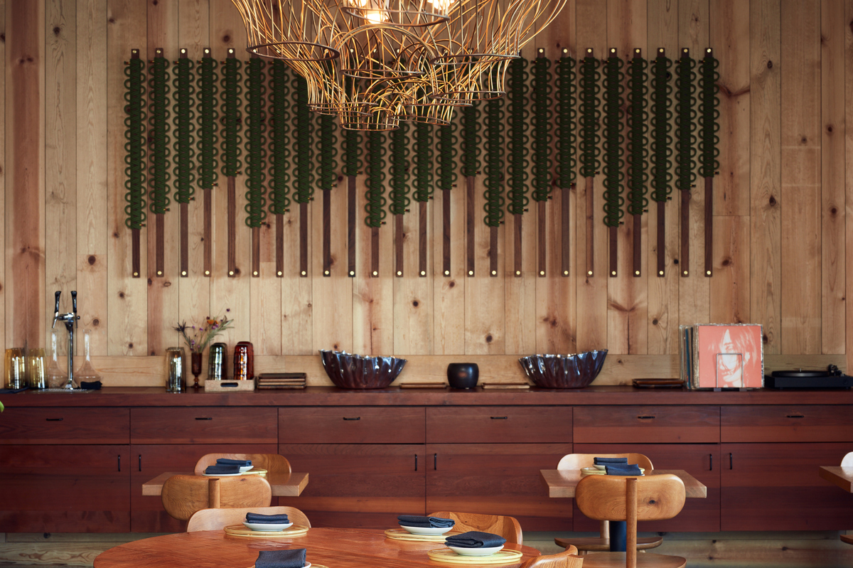 A long woodenchest running across the whole wood-paneled wall, a geometric light fixture and wooden tables.