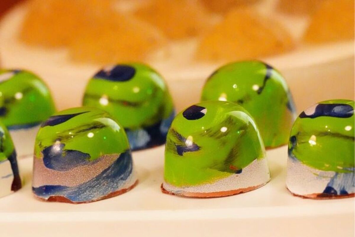 Glossy rounded green, sparkly and black chocolates.