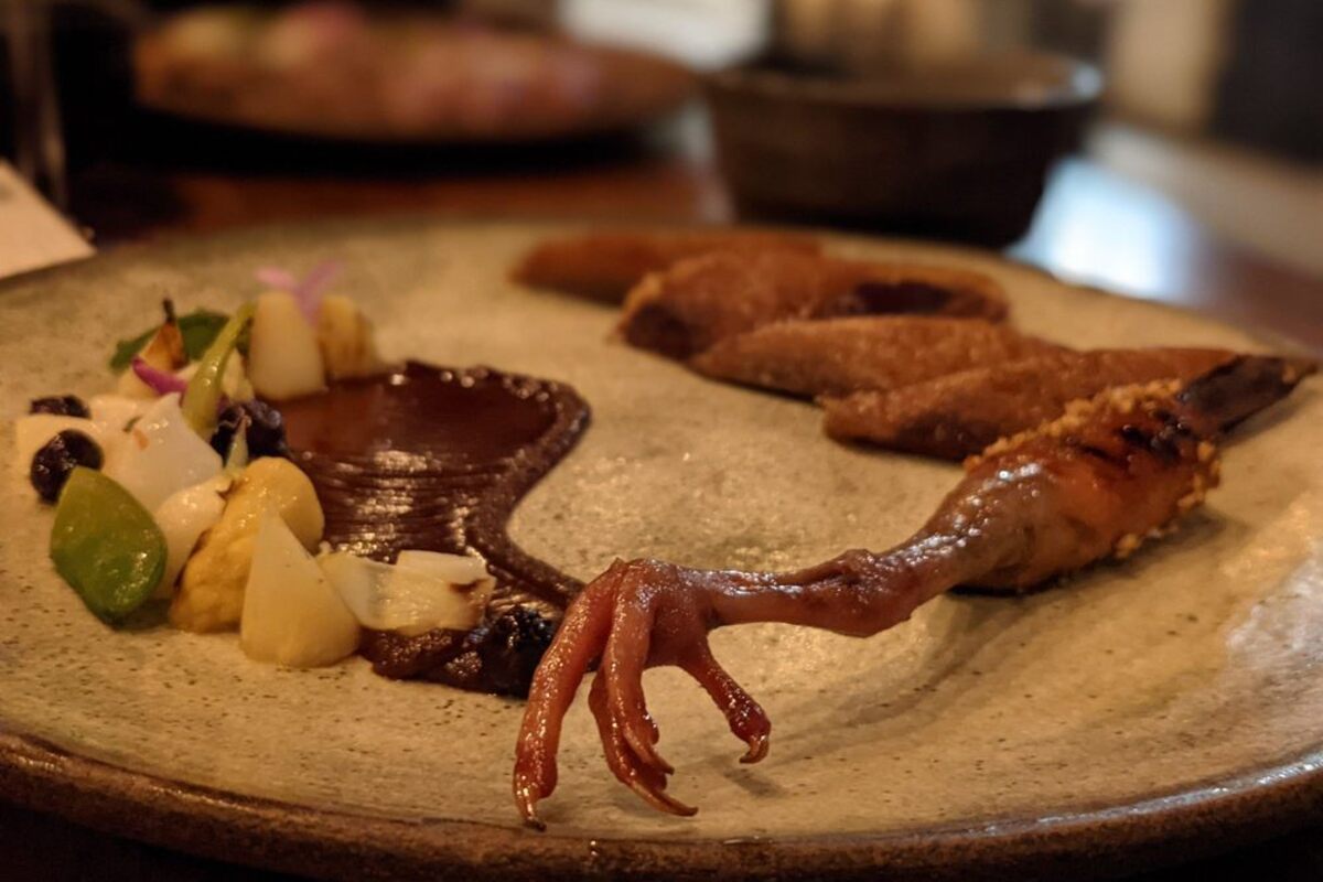 A chicken foot on a plate with small veggies and sauce.