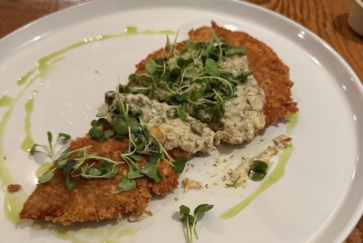 A white plate with breaded fried chicken topped with a white sauce and microgreens.