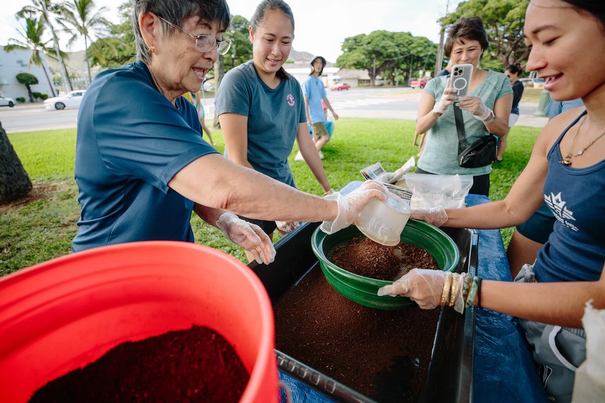 People hold a pan with clay above a tray and bucket of the material.