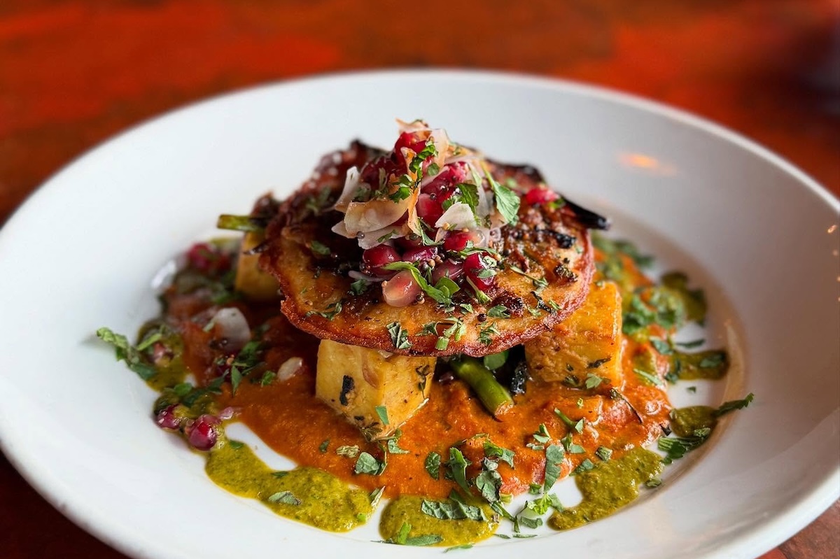 A plate with butternut squash uttapam, tofu paneer, caramelized onion, ciliantro chutney, pomegranate seeds and toasted coconut sambal.