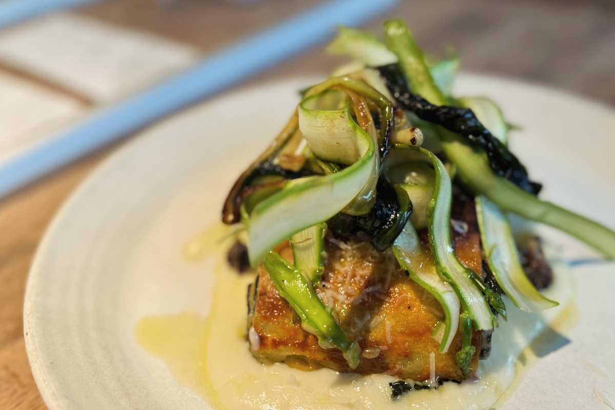 A morel mushroom and spinach lasagna top with shaved asparagus and sitting in some sauce.