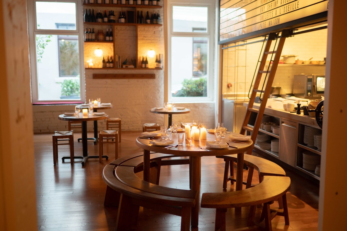Round tables with round benches around them decorated with lit candles, a set up with alcohol behind it and a decorative ladder.