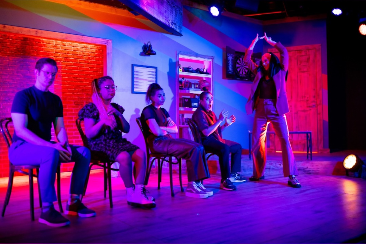 People sit in chairs onstage, lit with neon red, purple and blue hues.