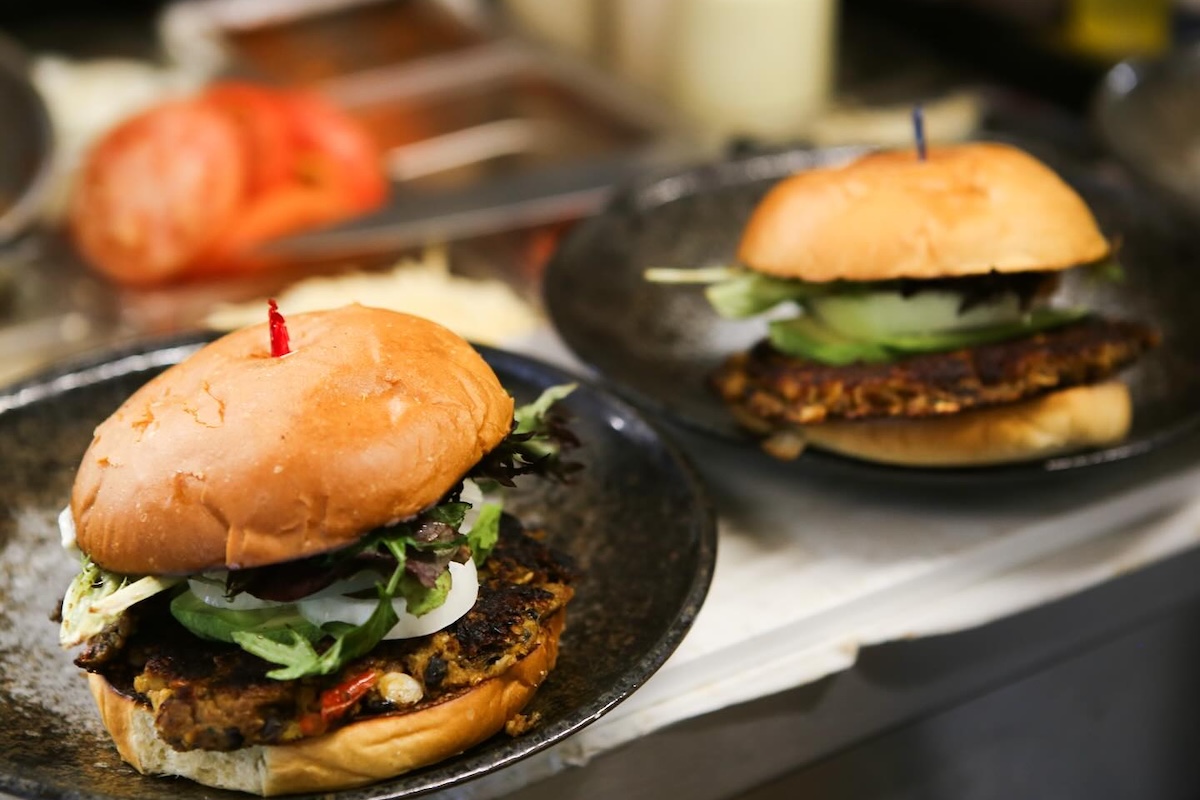 Two veggie burgers loaded with toppings and skewered with toothpicks sits on a tray.