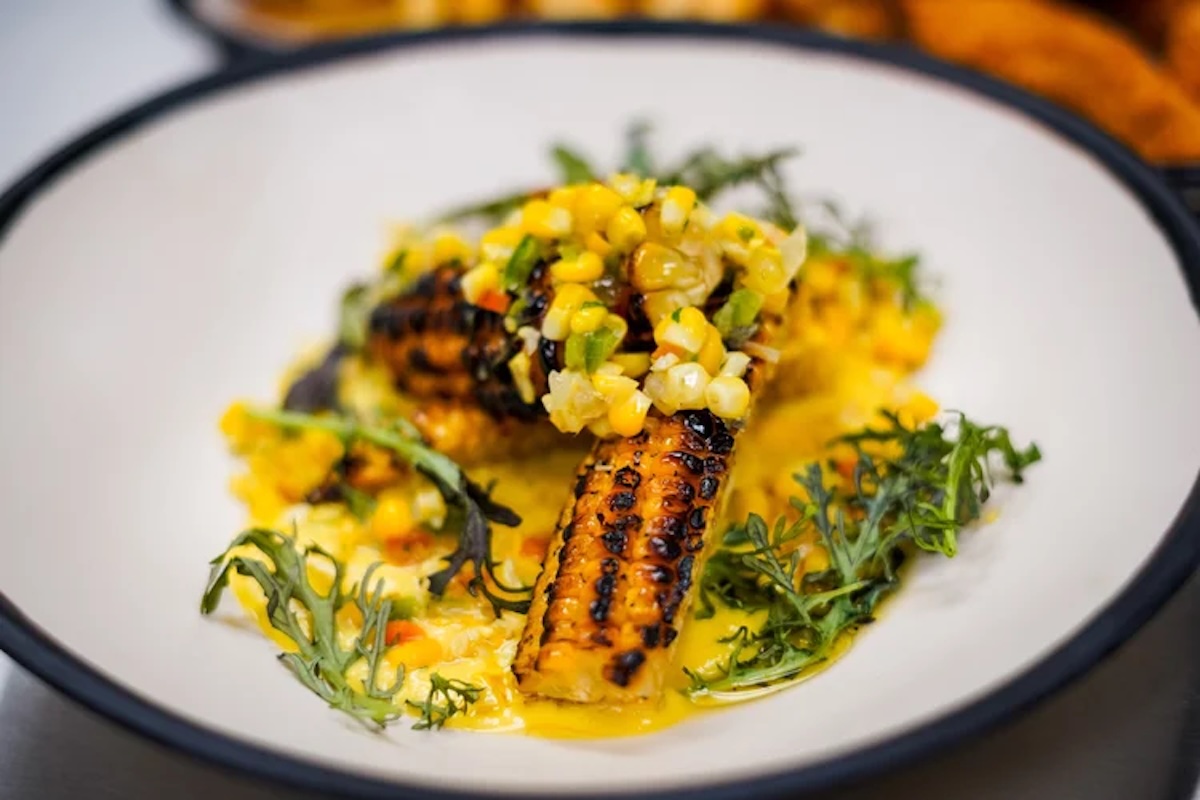 A plate with a bright yellow sauce, roasted corn and herbs.