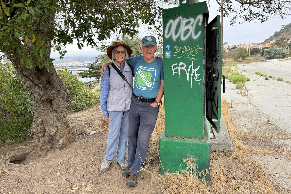 A couple stands next to a green metal fixture outside.