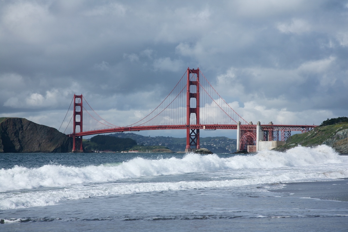 A view of the Golden Gate Bridge from Baker Beach, with the waves crashing on shore.