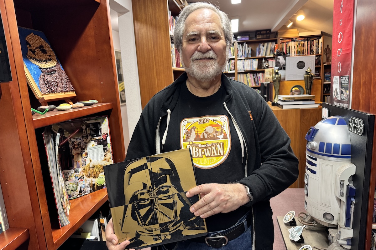 A man holds his first authored book called "Srar Wars: From Conceot to Screen to Collectible."