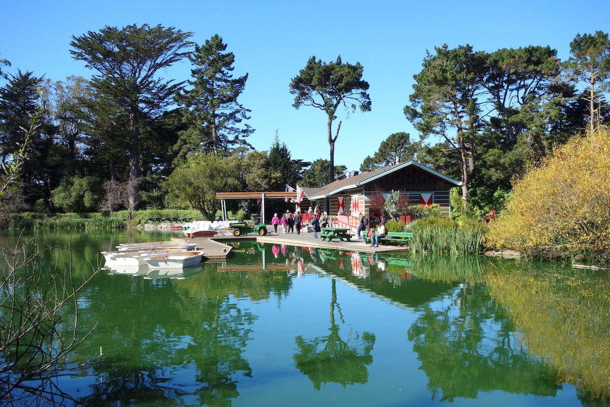 A boathouse on a lake with a dock that leads into green water and is surrounded by trees.
