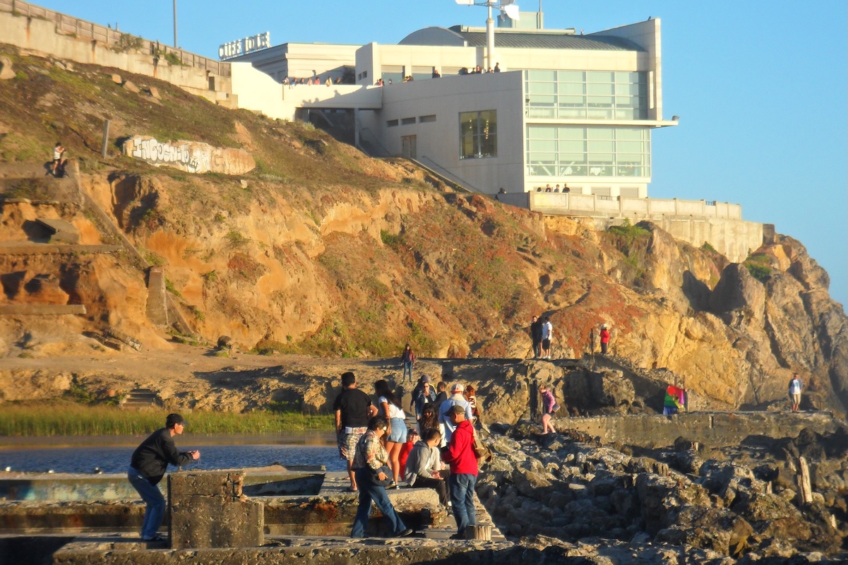 A view of the Sutro Baths along the coast and a white building in the cliff in the back.