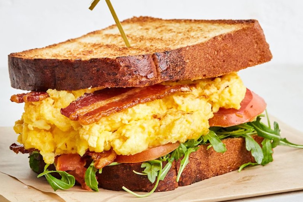 A sandwich with bacon, scrambled eggs, tomato and lettuce.
