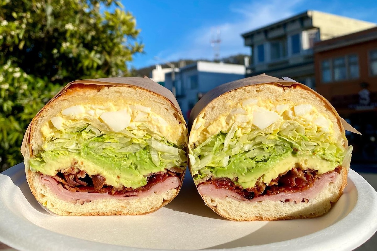 Two halves of a sandwich with egg salad, avocado, lettuce and meat.