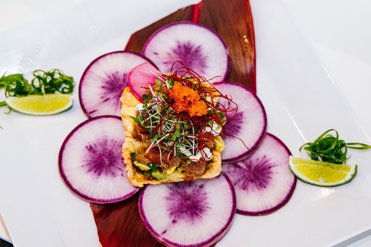 A plate with sliced veggies with a purple center, arranged around a mini pile of poke topped with microgreens, saffron, roe and more.