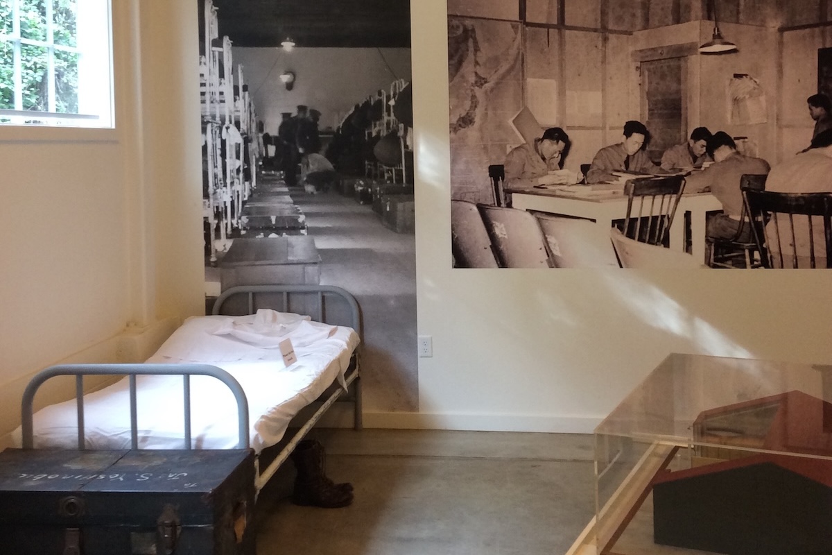 A twin sized bed sits in the corner of a historical room with posters in black and white hanging on the wall behind.