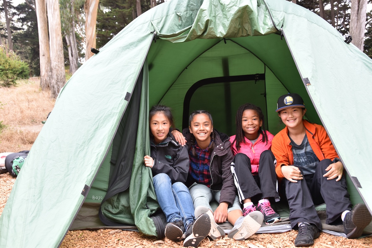 A group of four kids sit inside a green camping tent.