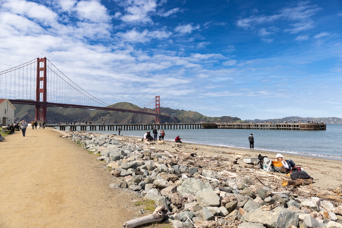 A view of the Golden Gate Bridge and part of the bay from a dirt path lined with rocks.