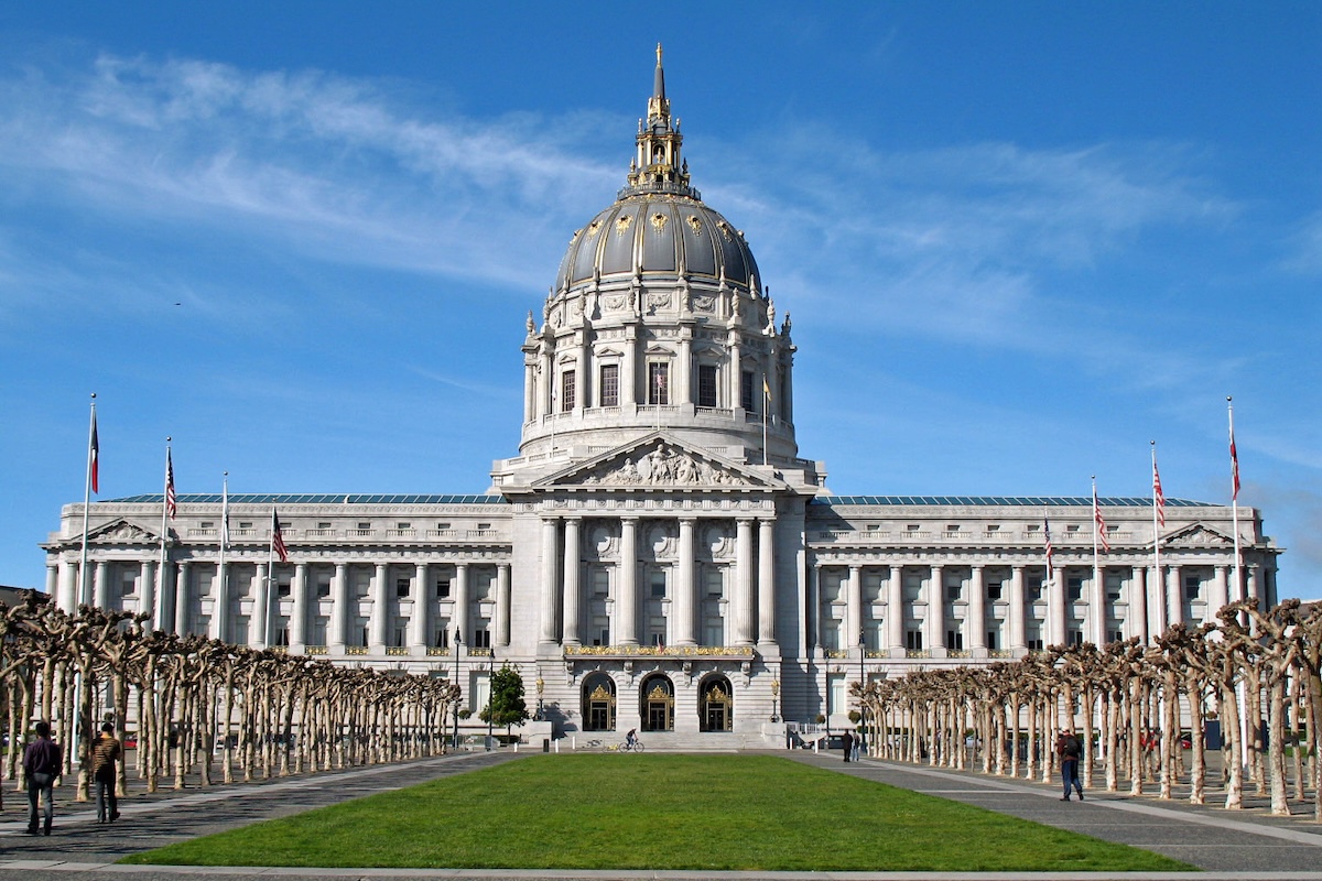 A view of San Francisco City Hall, with a grassy field leading to the entrance and a blue sky.