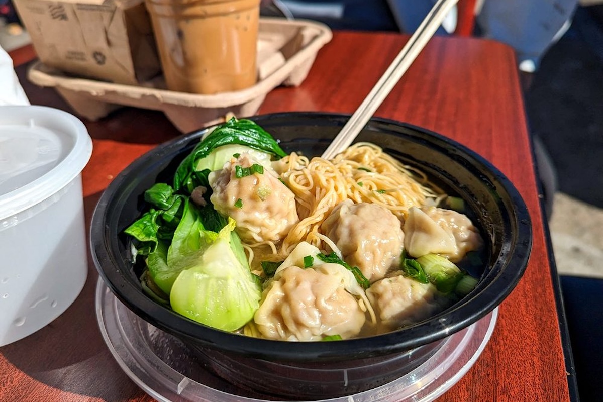 A black plastic bowl of noodles, dumplings and veggies.