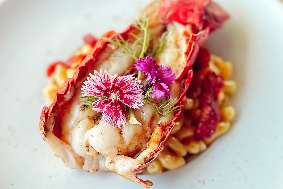 A crustacean with meat, topped with herbs and edible pink flowers.