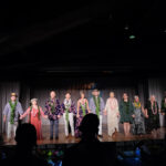 A group of people in Hawaiian attire stand hand in hand on stage during a ceremony