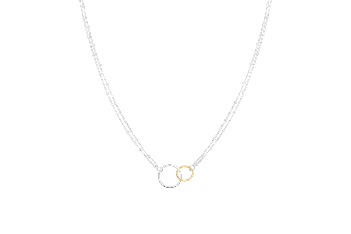This image features a silver chain necklace with two interlocking circles, a large silver circle and a smaller gold circle.
