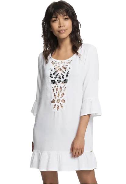 climate-friendly-beach-cover-up-roxy-longsleeve-dress-@amazon A woman with shoulder-length hair is wearing a three-quarter sleeve white dress, designed as one of those climate-friendly beach cover ups, featuring a delicate lace pattern on the front and a ruffled hem. She stands against a plain background, looking forward with a slight smile and one hand resting by her side.